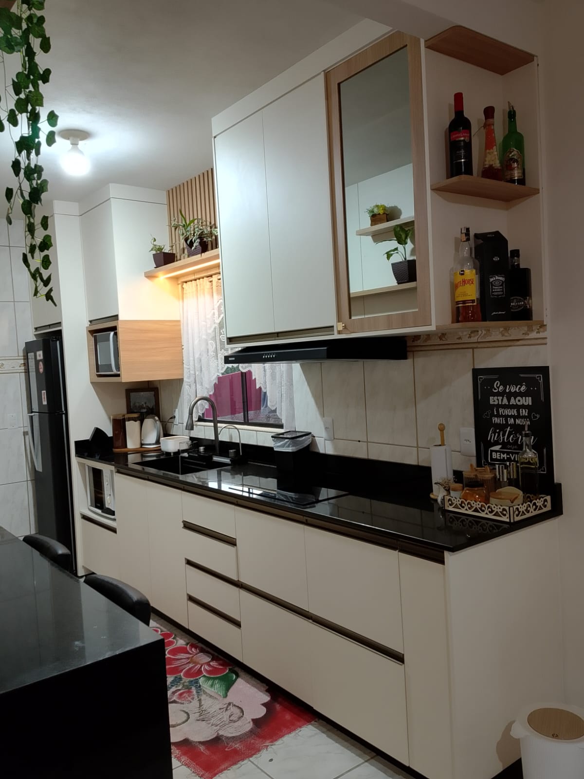 Cozinha planejada branca com detalhes amadeirados, cristaleira e bancada preta